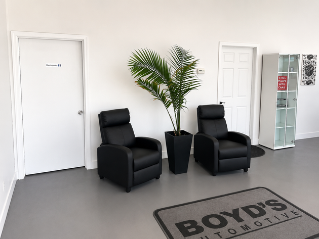 Bright lobby with two black armchairs, potted plant, doors, and a glass display cabinet.