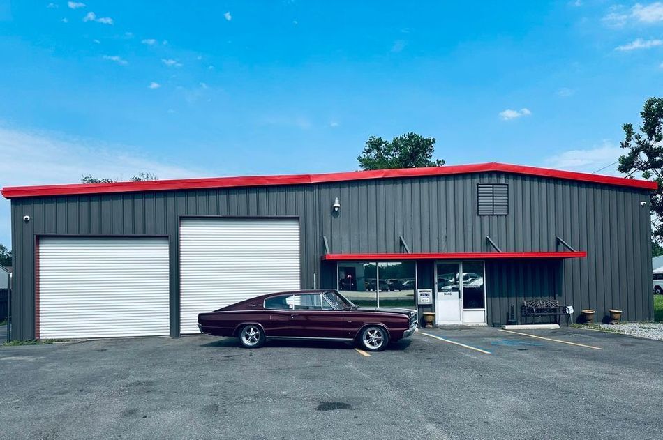 A burgundy Mustang is parked in front of an auto repair shop.