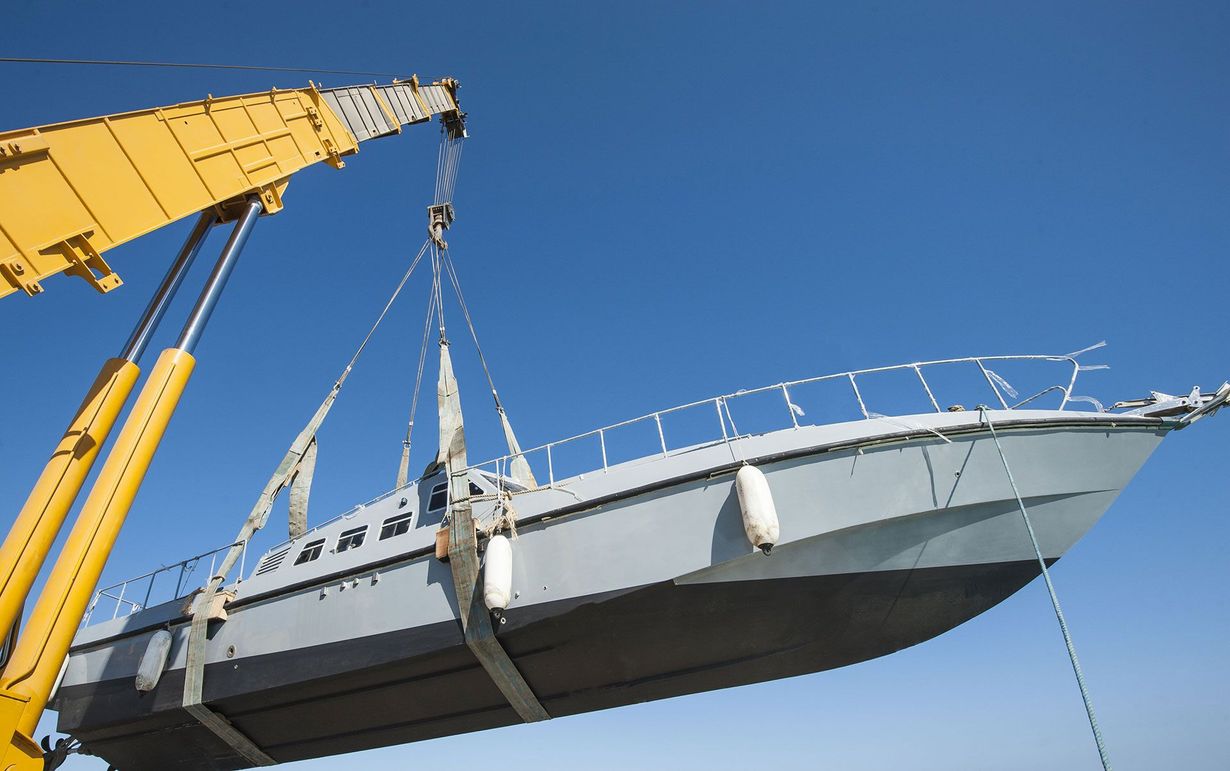 Crane lifting a gray boat against a clear blue sky.