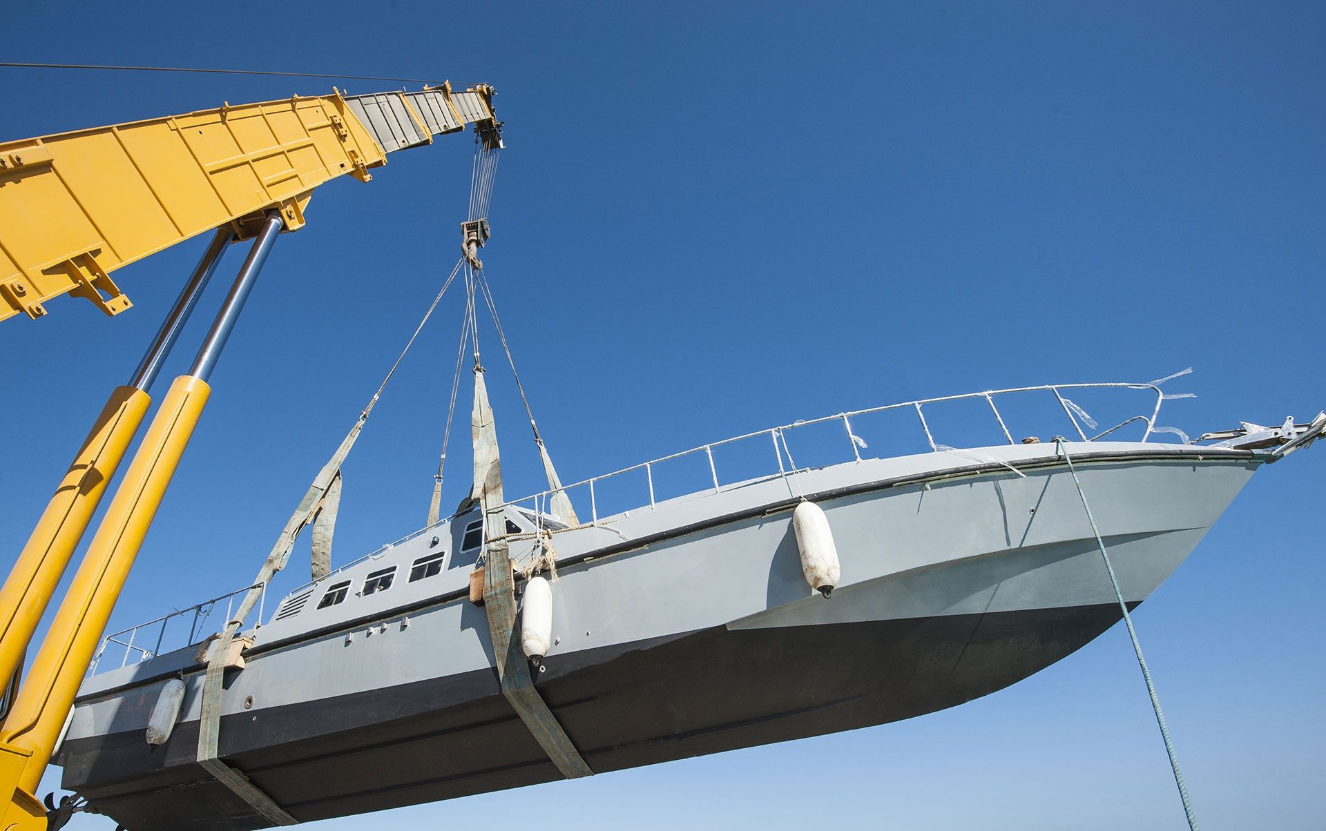 Crane lifting a gray boat against a clear blue sky.