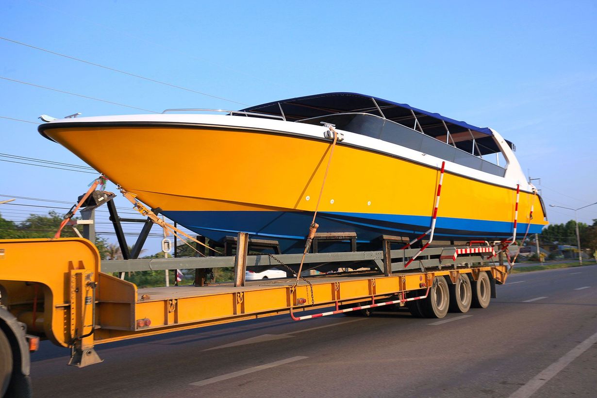Yellow and white speedboat on a flatbed trailer, being transported on a road. Blue sky in the background.