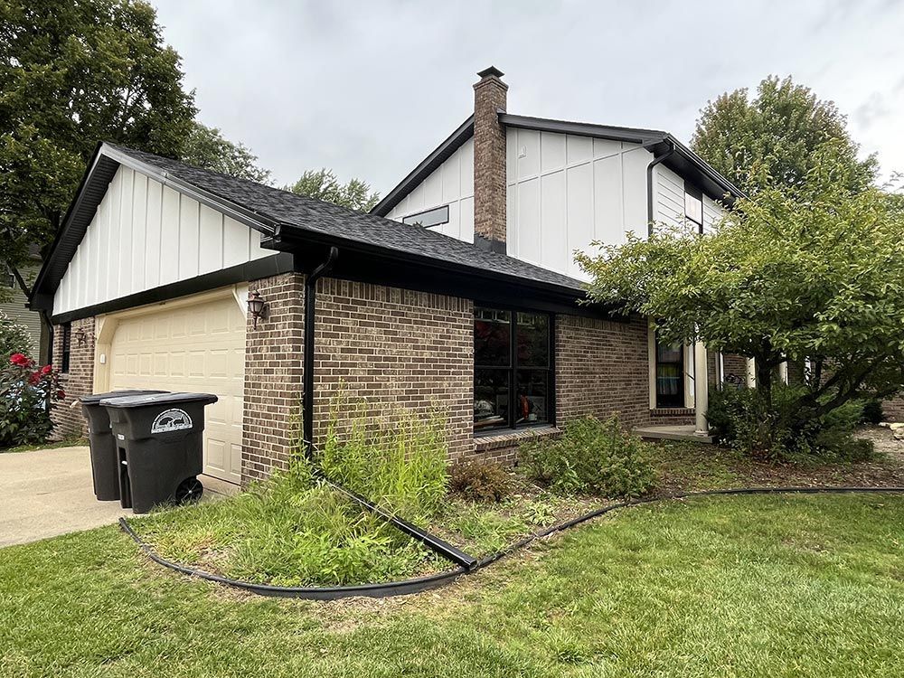 A brick house with a white garage door and a black trash can in front of it.