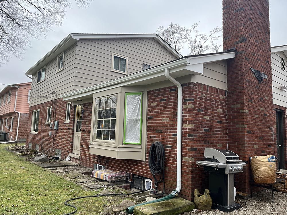 The back of a brick house with a barbecue grill in the backyard.