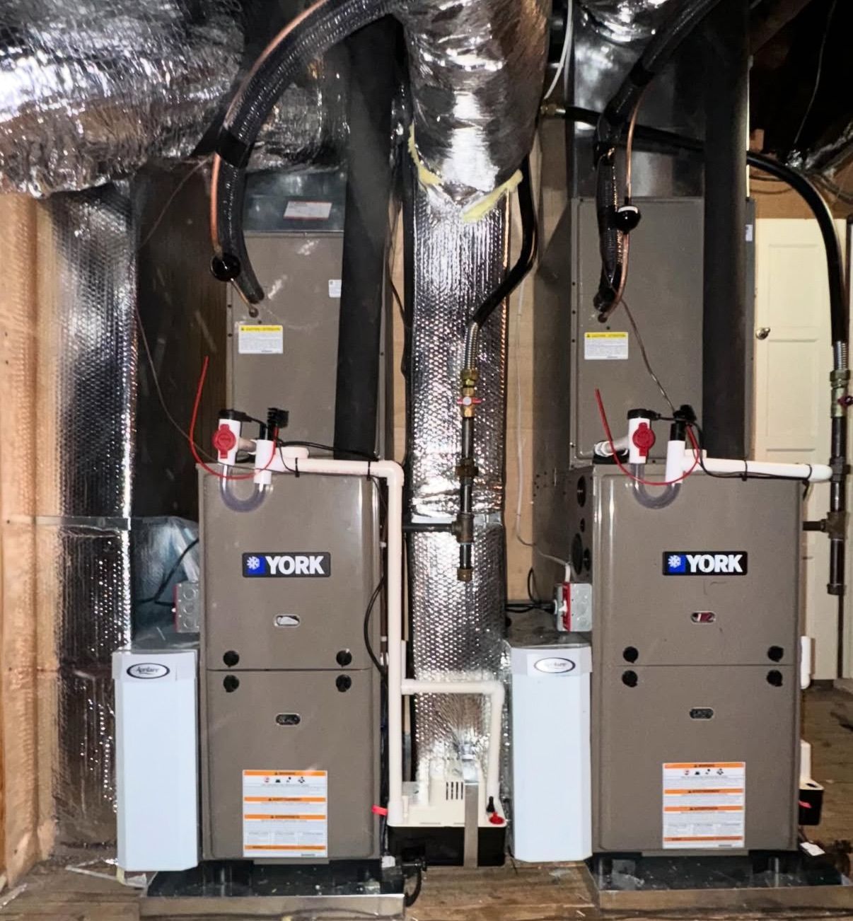 Two York HVAC furnaces installed side-by-side in a mechanical room with ductwork, piping, and condensate pumps