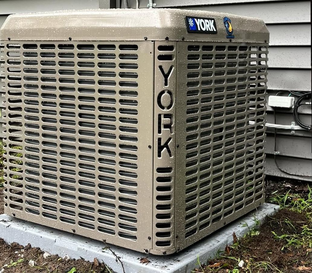 An outdoor air conditioning condenser unit sitting on a concrete pad against house siding