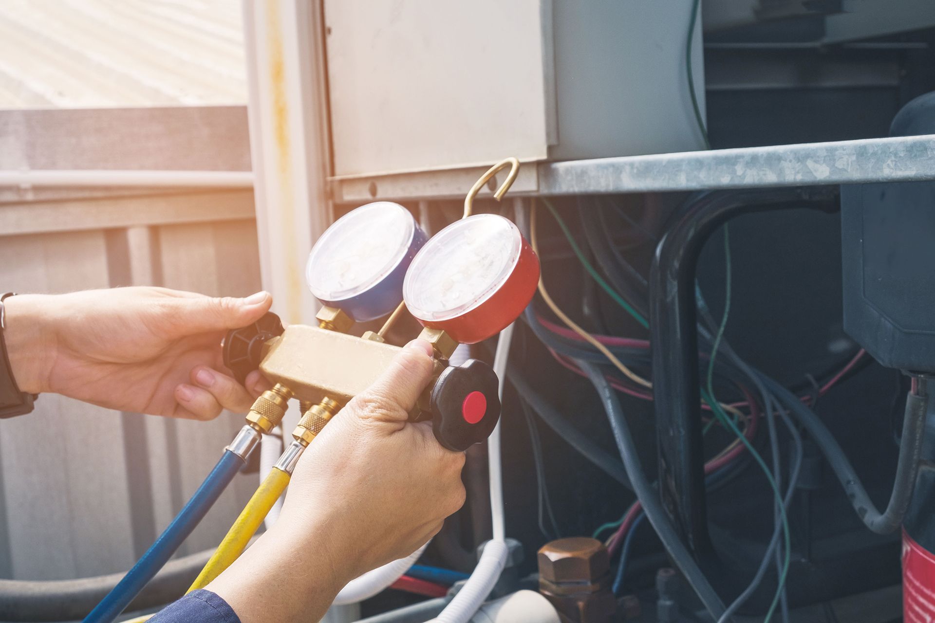 A technician uses a red and blue HVAC manifold gauge set to service an outdoor air conditioning unit