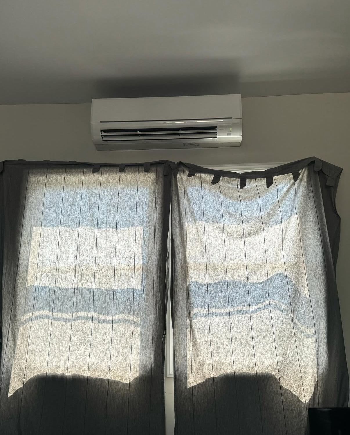 A white air conditioning unit mounted on a light wall a window