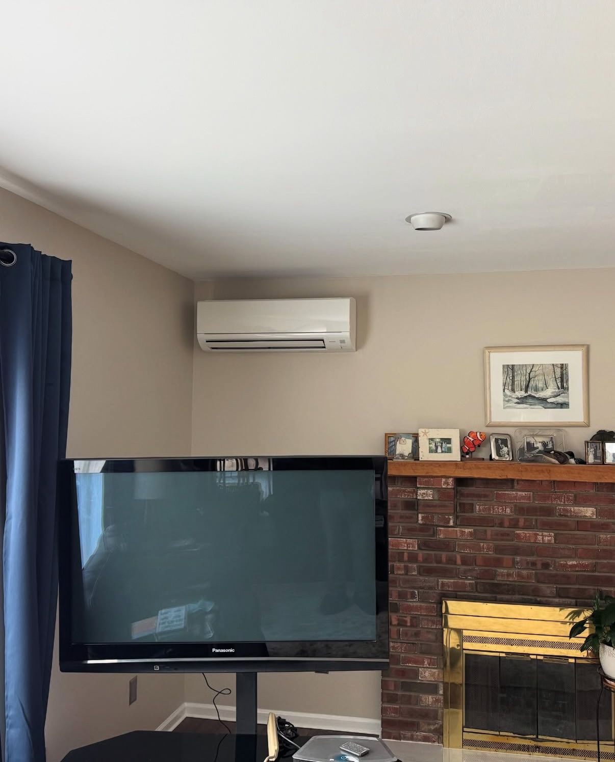 A living room corner features a wall-mounted AC unit above a television on a stand