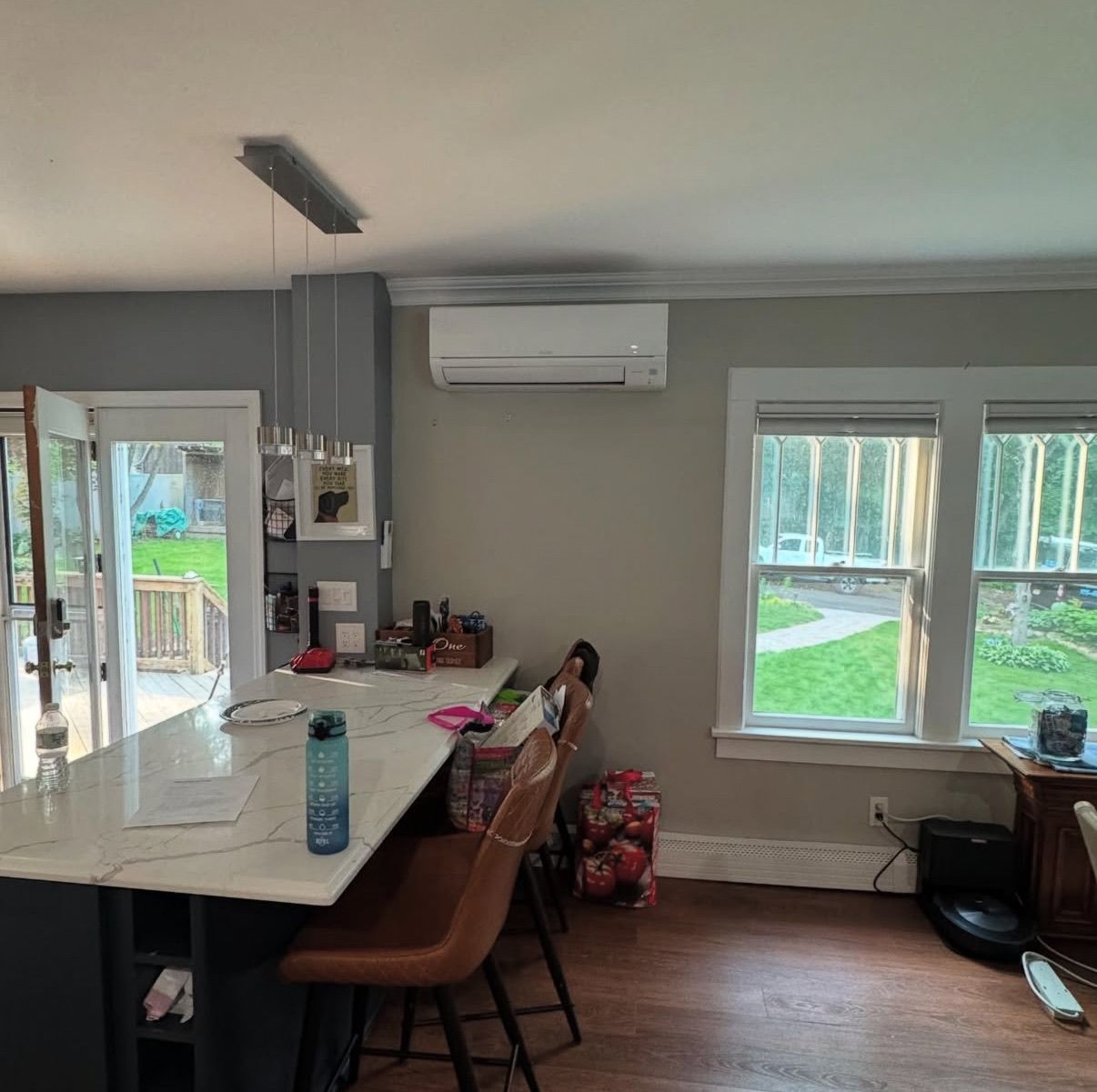 A bright kitchen featuring a white marble island with brown chairs and a wall-mounted AC unit