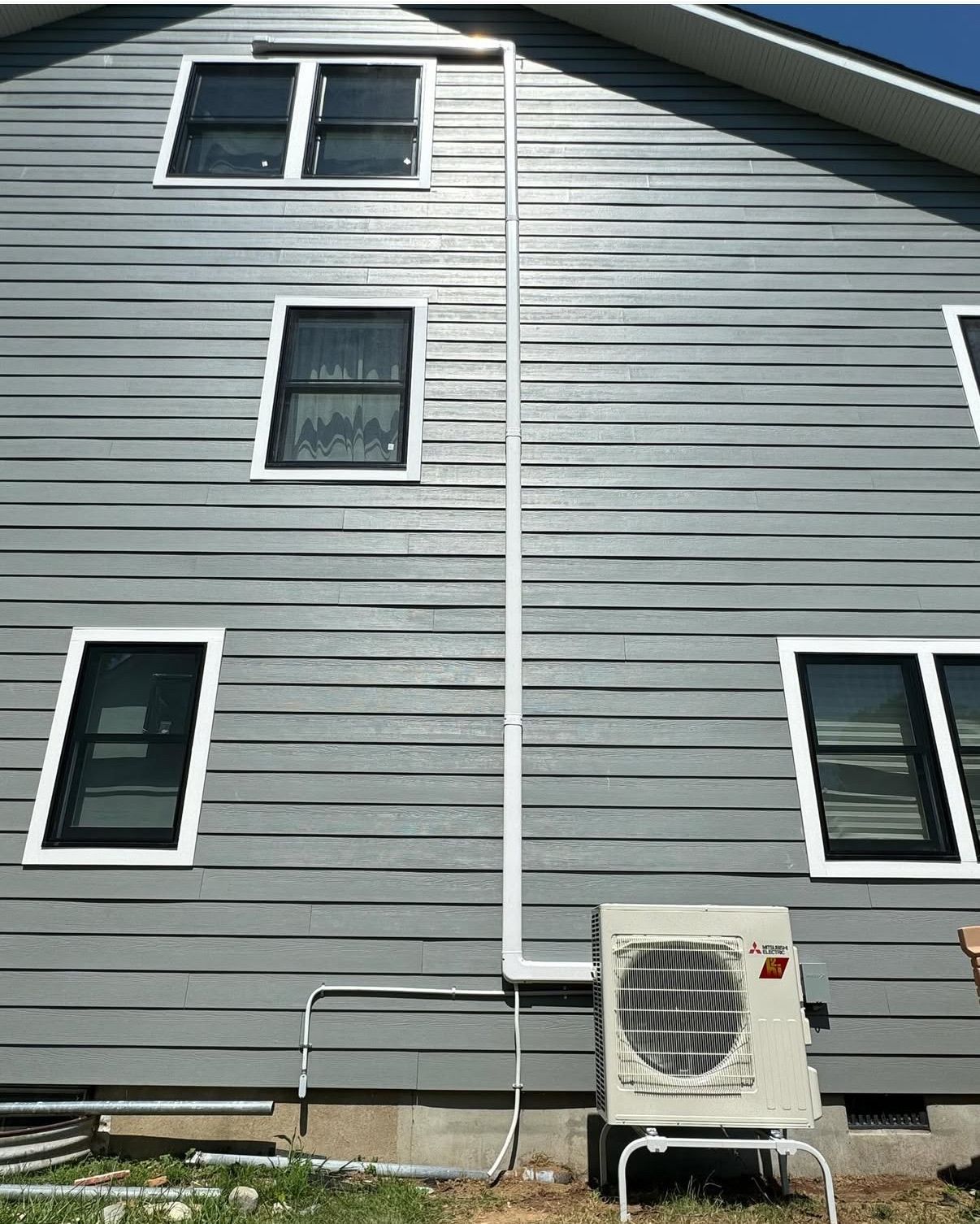 White Mitsubishi outdoor HVAC unit connected to vertical conduit piping.