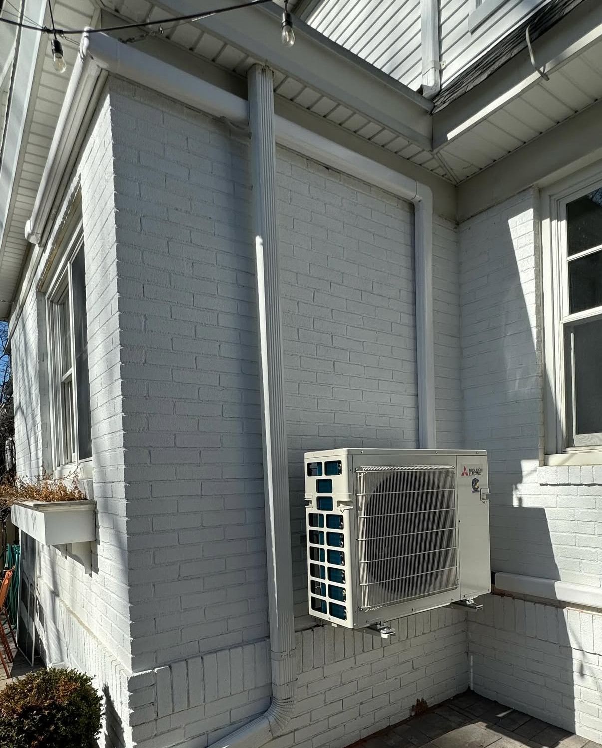 An outdoor HVAC unit mounted next to a vertical drainpipe