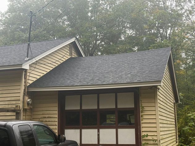 A sagging roof on a tan, wooden garage exterior with a dark-framed garage door and shingles.