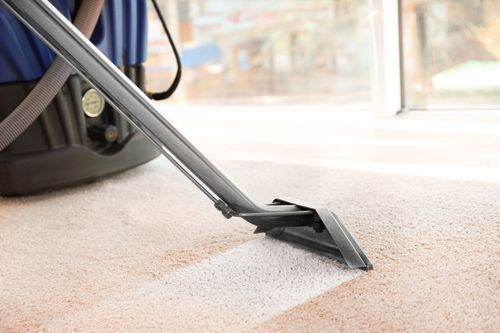 Vacuum cleaner nozzle removing dust from a carpet near a window