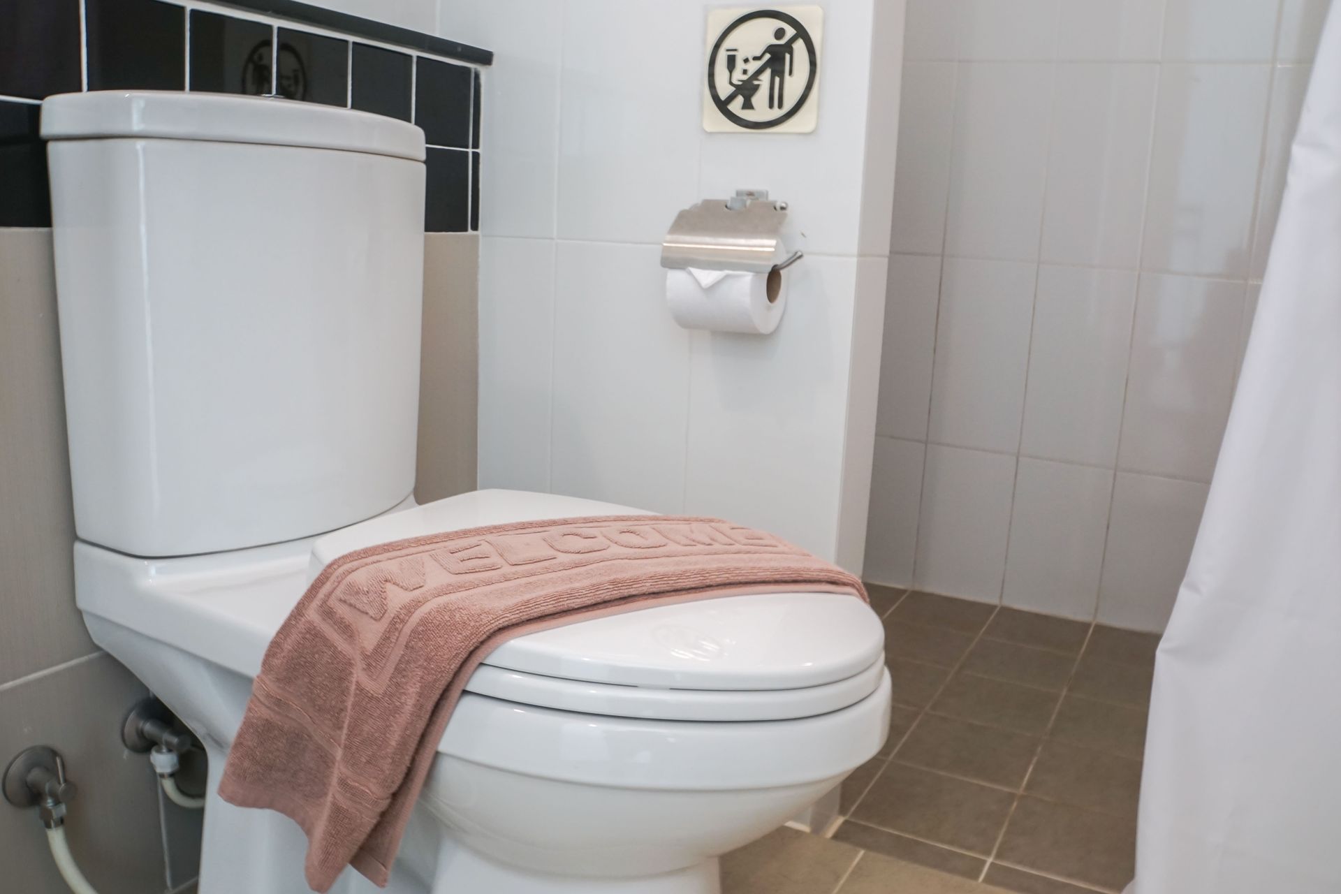 Bathroom with a white toilet and pink towel draped over the seat, next to a wall-mounted toilet paper holder.