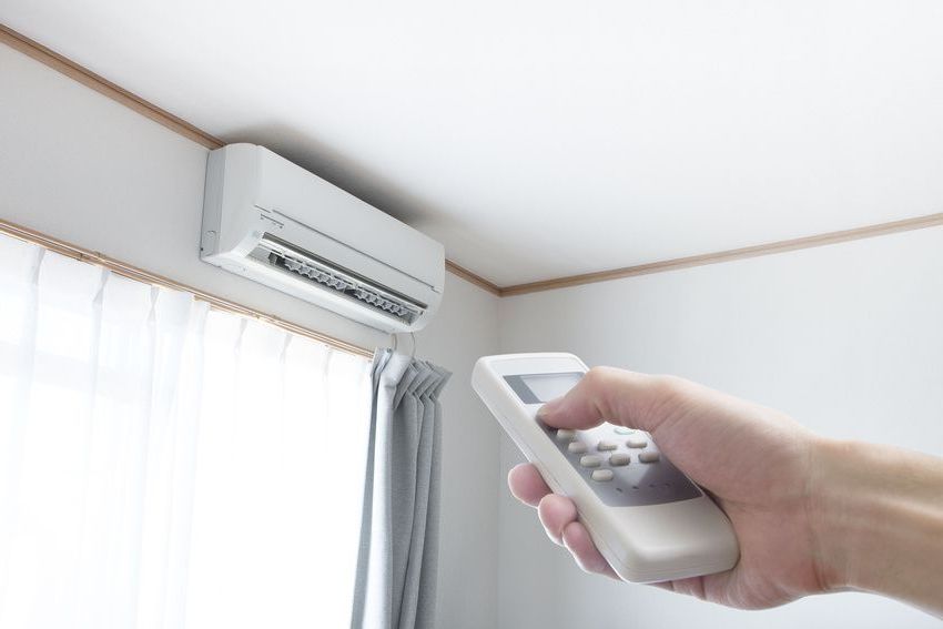 A person is holding a remote control in front of an air conditioner