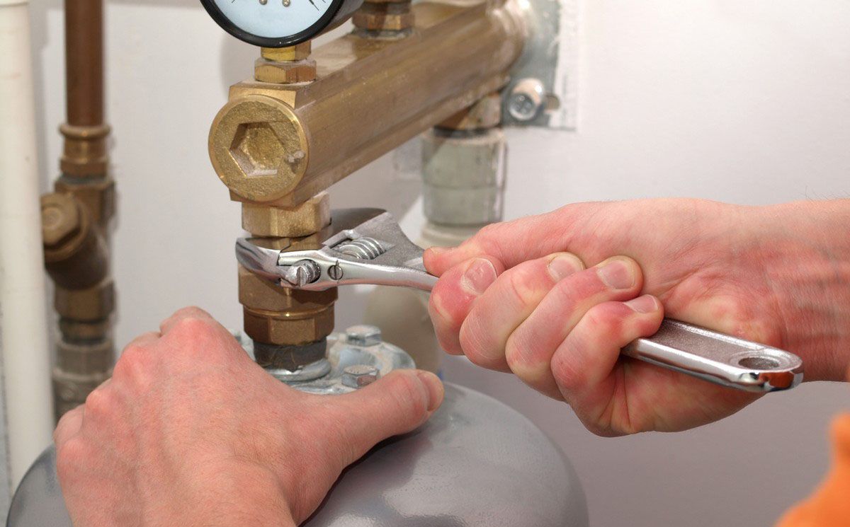 A person is fixing a water heater with a wrench.