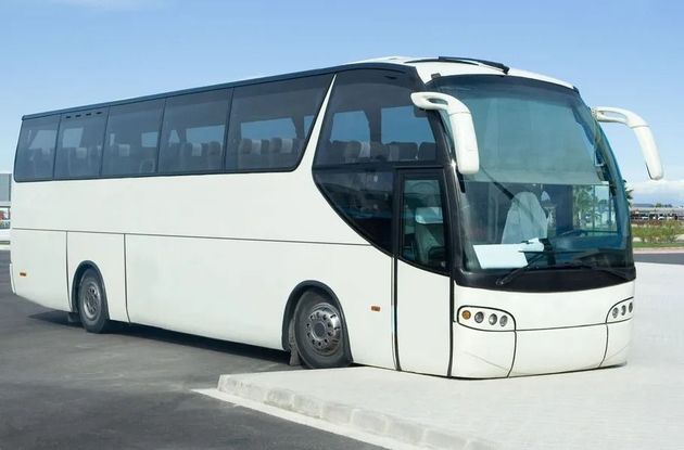 White coach bus parked on pavement, angled front view, with dark tinted windows and blue sky background