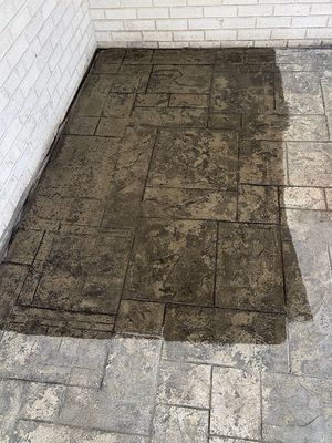 Stained concrete patio with rectangular stone pattern next to a white brick wall.