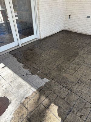 Stamped concrete patio, mostly wet, next to a brick wall and glass door.