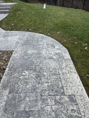 Gray stamped concrete walkway curves along a grassy yard.
