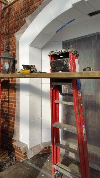 Red ladder near white archway under construction, next to brick wall. Tools on shelf.
