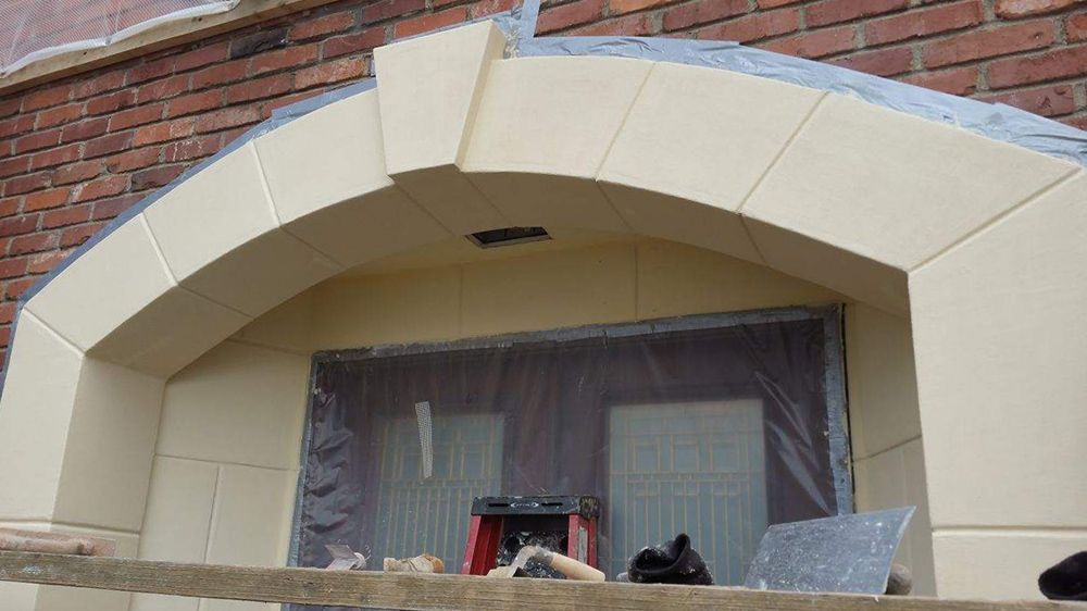 Stone archway over a window on a brick building, under construction. Beige stone, plastic covered window.