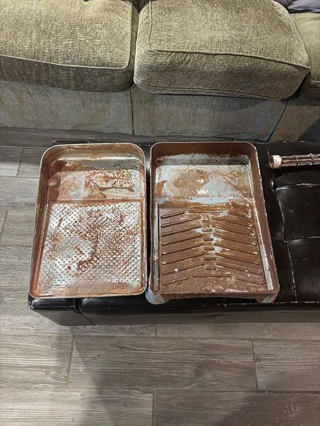 Two rusty paint trays on a brown leather surface next to a tan couch.