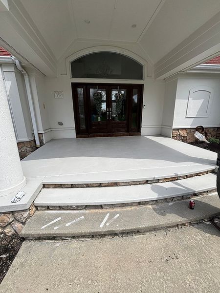 Front porch with a light gray concrete surface, steps, and a brown front door under a white overhang.