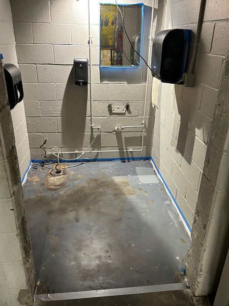 Basement bathroom, concrete walls, with toilet, paper towel dispensers, and pipes.