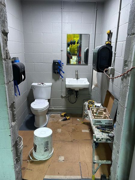 Small, unfinished restroom with a toilet, sink, and work table; tools scattered. Walls are gray.