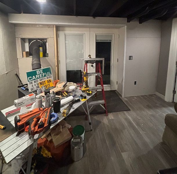 Basement construction site with tools on a table, unfinished walls, doorway, and new flooring.