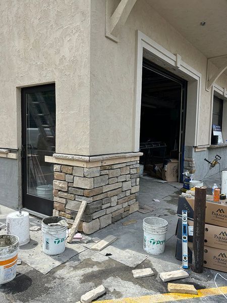 Building exterior with stone veneer and a partially open garage door. Construction tools and materials are scattered nearby.