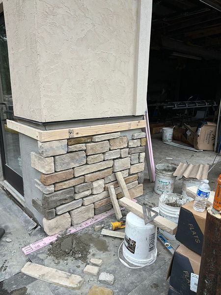 Stone veneer installation on a building column. A worker is using tools to set the stones.