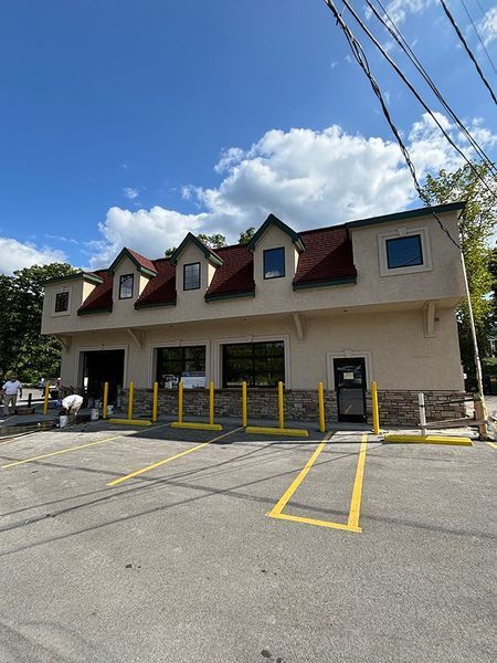 Two-story beige building with brown roof and dormers. Yellow parking lines. Blue sky with clouds.