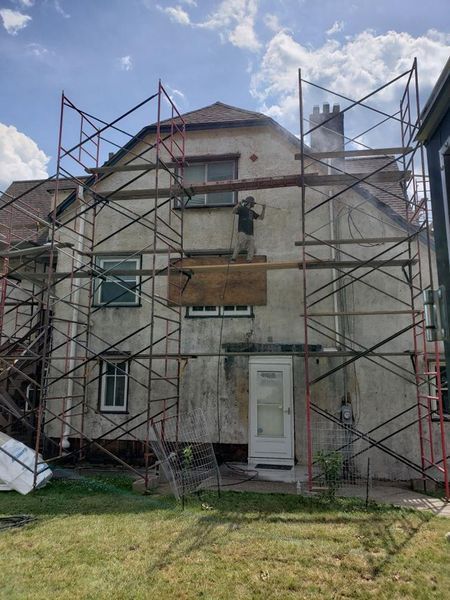 A person on scaffolding working on the exterior of a two-story building, sunny day.