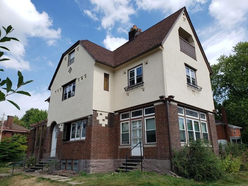 Two-story brick and stucco house with brown roof, white trim, and small balcony.