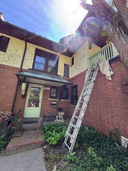 Exterior of a brick house with a ladder against the wall, painted yellow and red with a green door.