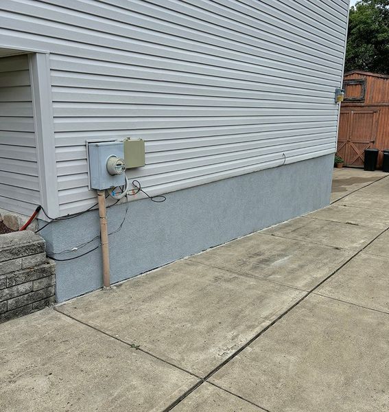 Gray concrete sidewalk next to a light blue house with gray concrete foundation.