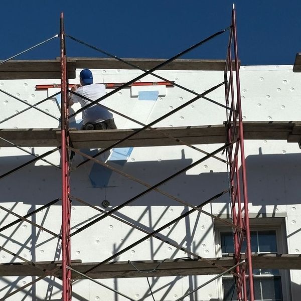 Construction worker on scaffolding applying insulation to building exterior.