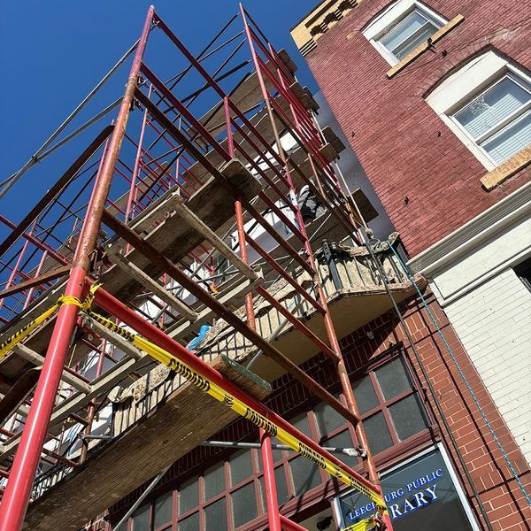 Red scaffolding on brick building. Yellow caution tape, sunny day.