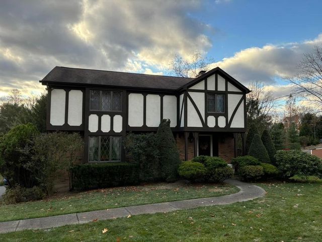 Two-story Tudor-style house with white and brown exterior, pathway leading to the front door, cloudy sky.