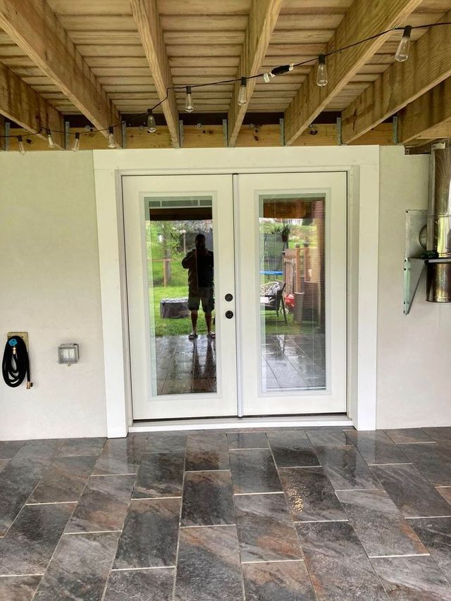 White French doors open to a backyard. A person is reflected in the glass. Stone tile flooring is in foreground.