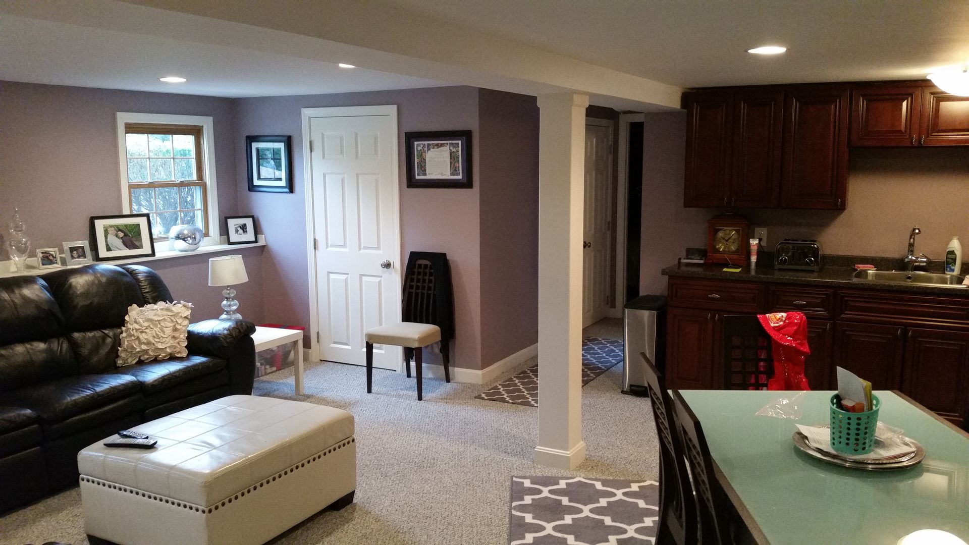A living room with a couch , ottoman , table and kitchen.