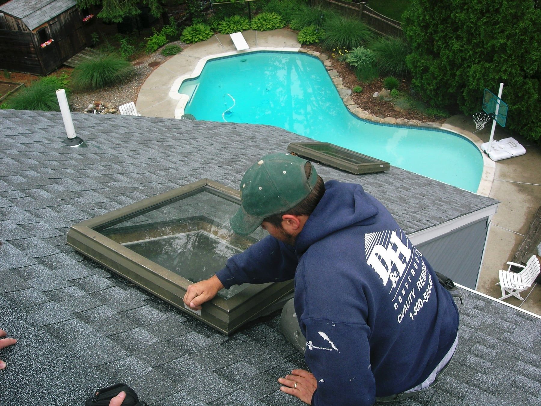 A man in a blue sweatshirt with the letter a on the back is working on a skylight