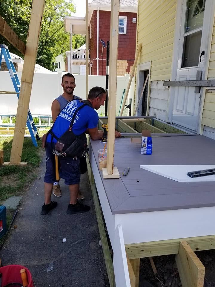 Two men are working on a porch in front of a house.