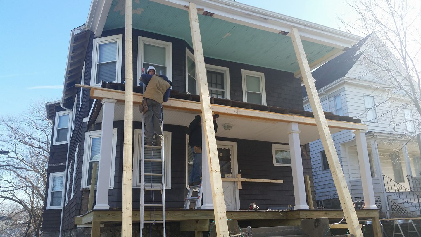 A man is standing on a porch of a house under construction.