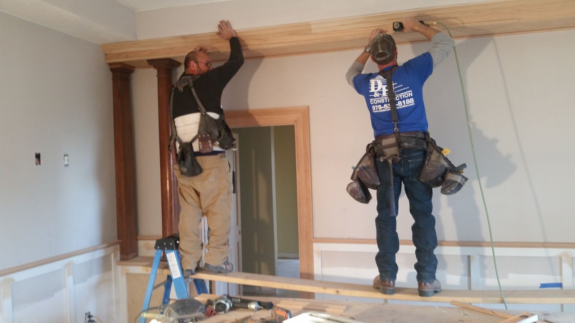 Two men are working on a wooden beam in a room.