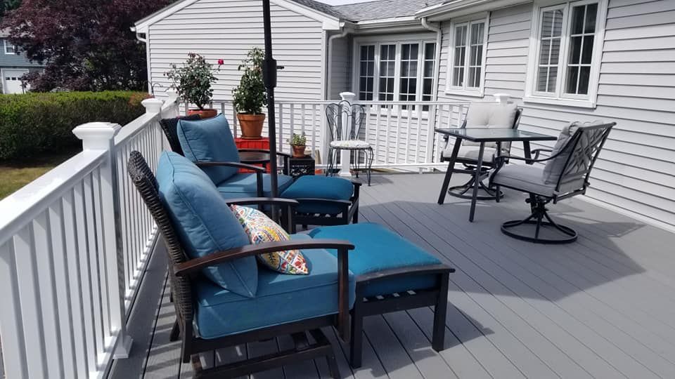 A deck with chairs , a table and an umbrella in front of a house.