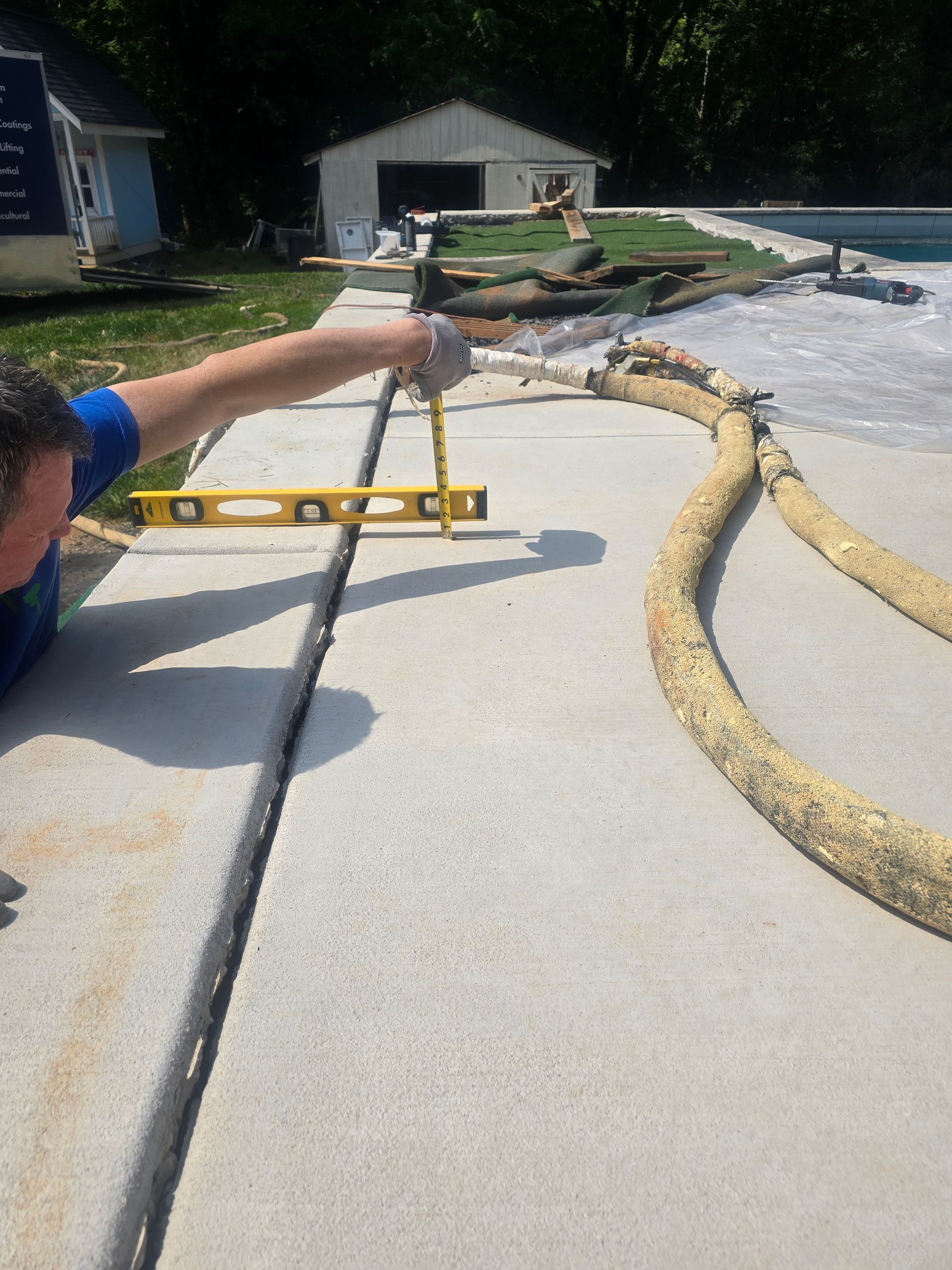 A person using a level to inspect a concrete walkway near a pool.