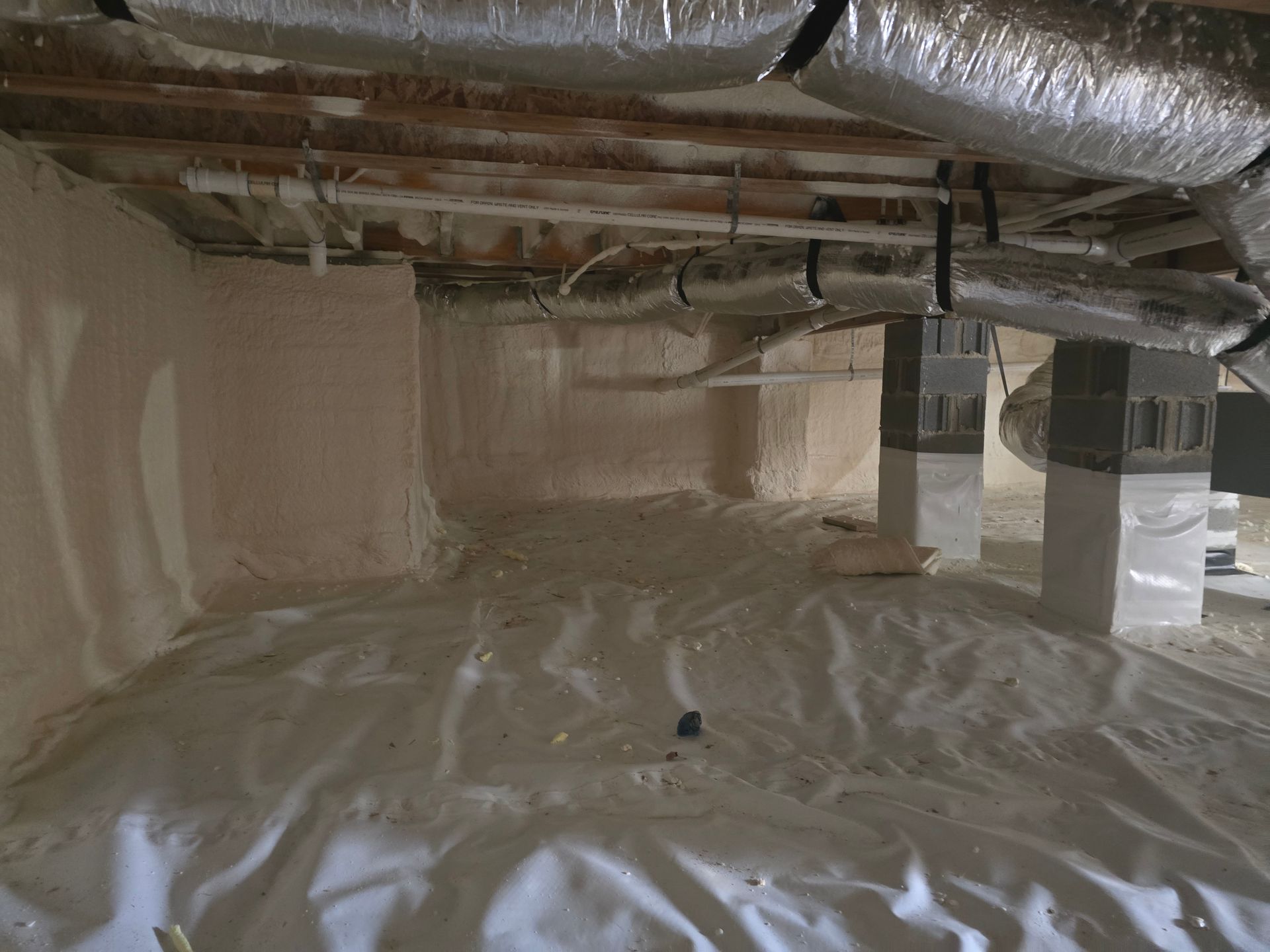 Crawl space with pink insulation on walls and ceiling, white vapor barrier on the ground, and support columns.